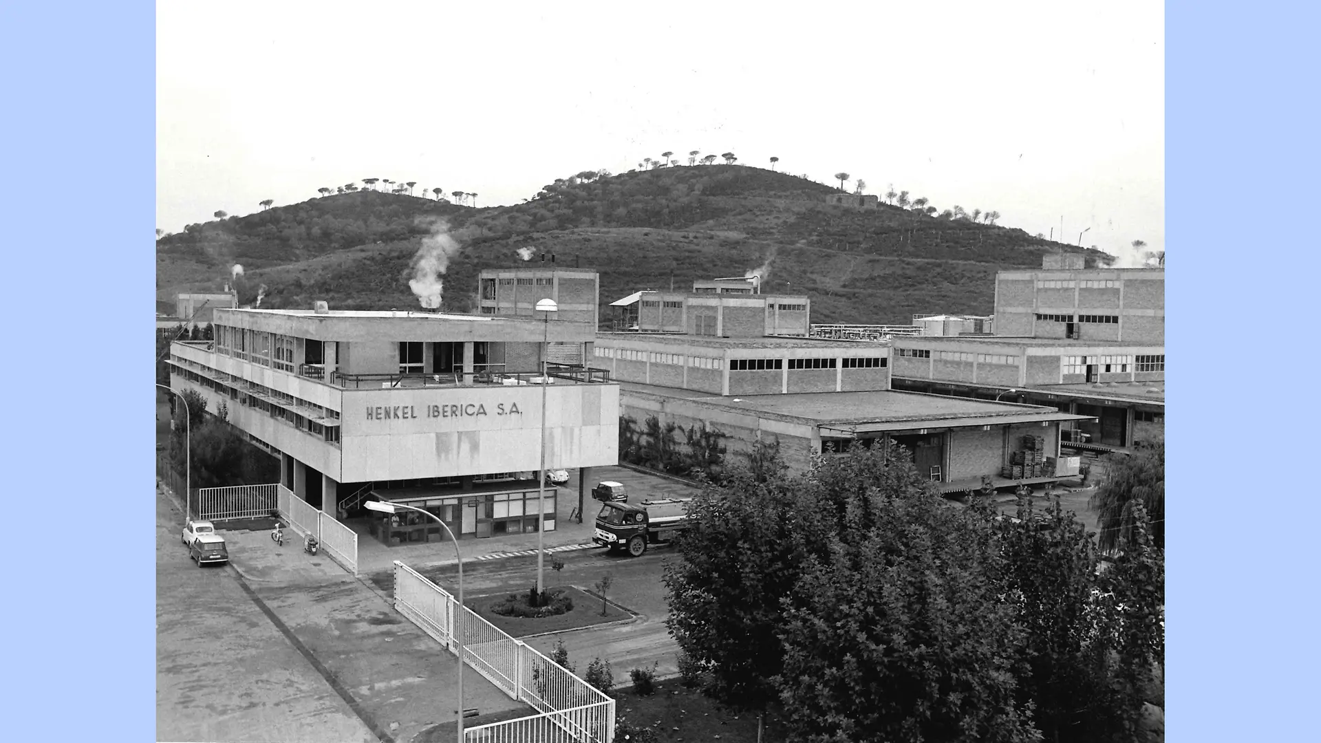 Imagen en blanco y negro del exterior de las instalaciones de Montornès. La fotografía muestra el complejo industrial con sus diversos edificios rodeados por las colinas y montañas de la zona.