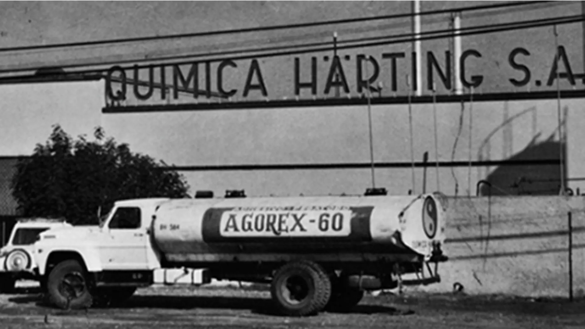 Vehículo de marca Agorex frente al edificio de Química Härting en blanco y negro.