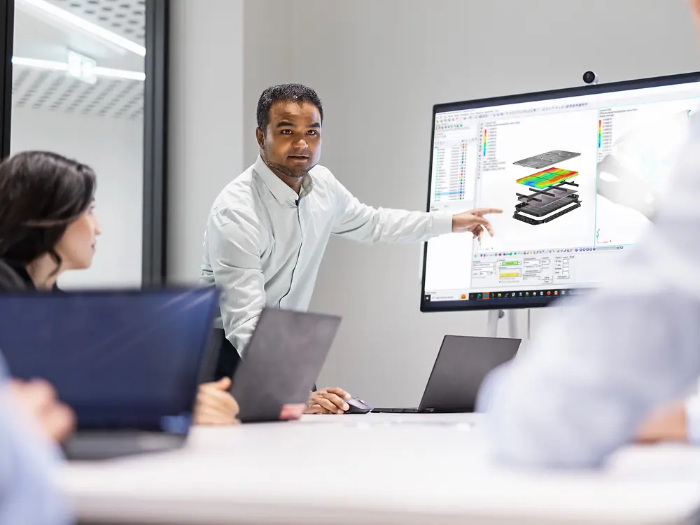 Equipo colaborando en innovación con soluciones Loctite, con un profesional presentando diseños de modelado y simulación en una pantalla grande durante una reunión técnica.