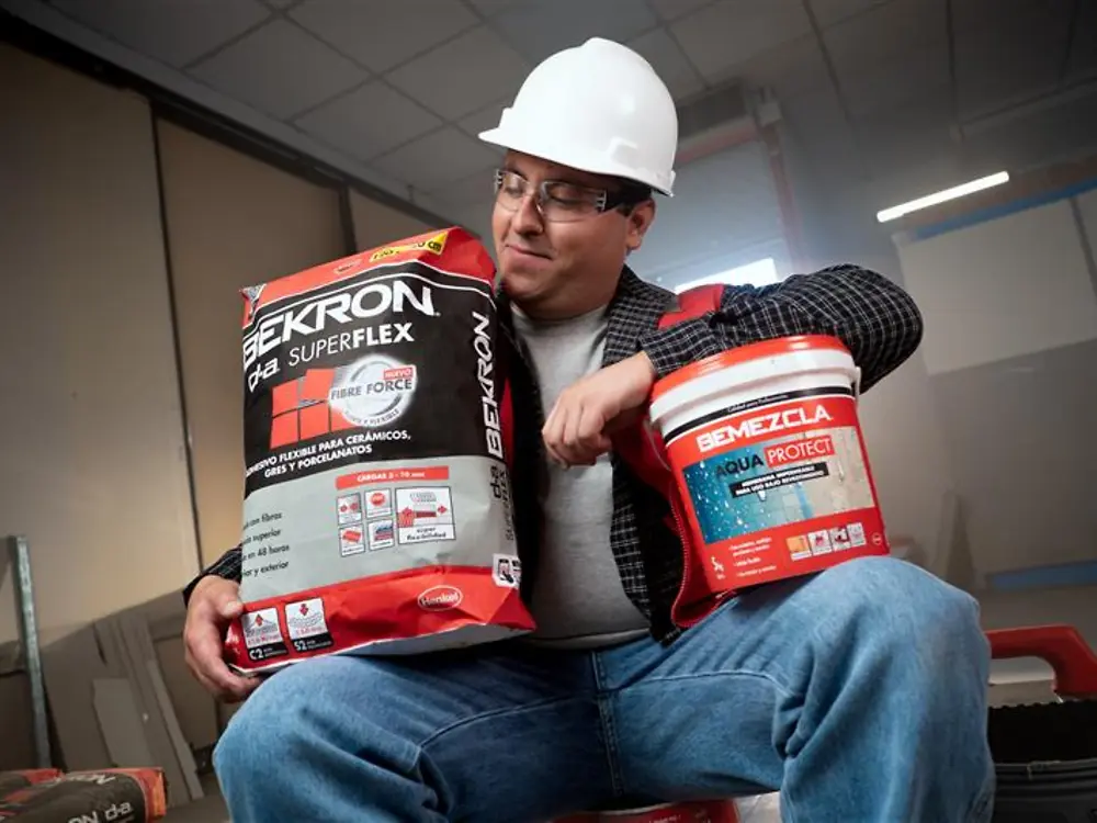 Maestro viste casco de seguridad, mientras sostiene felizmente su saco y tineta de Bekron.