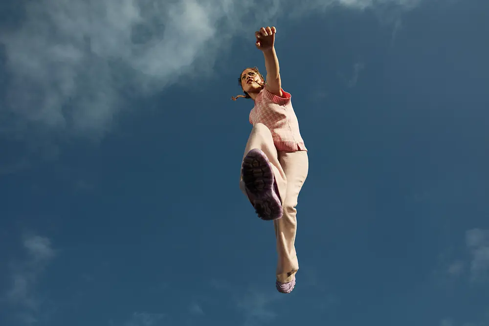 
A woman jumping enthusiastically over the camera with clear blue sky in the background