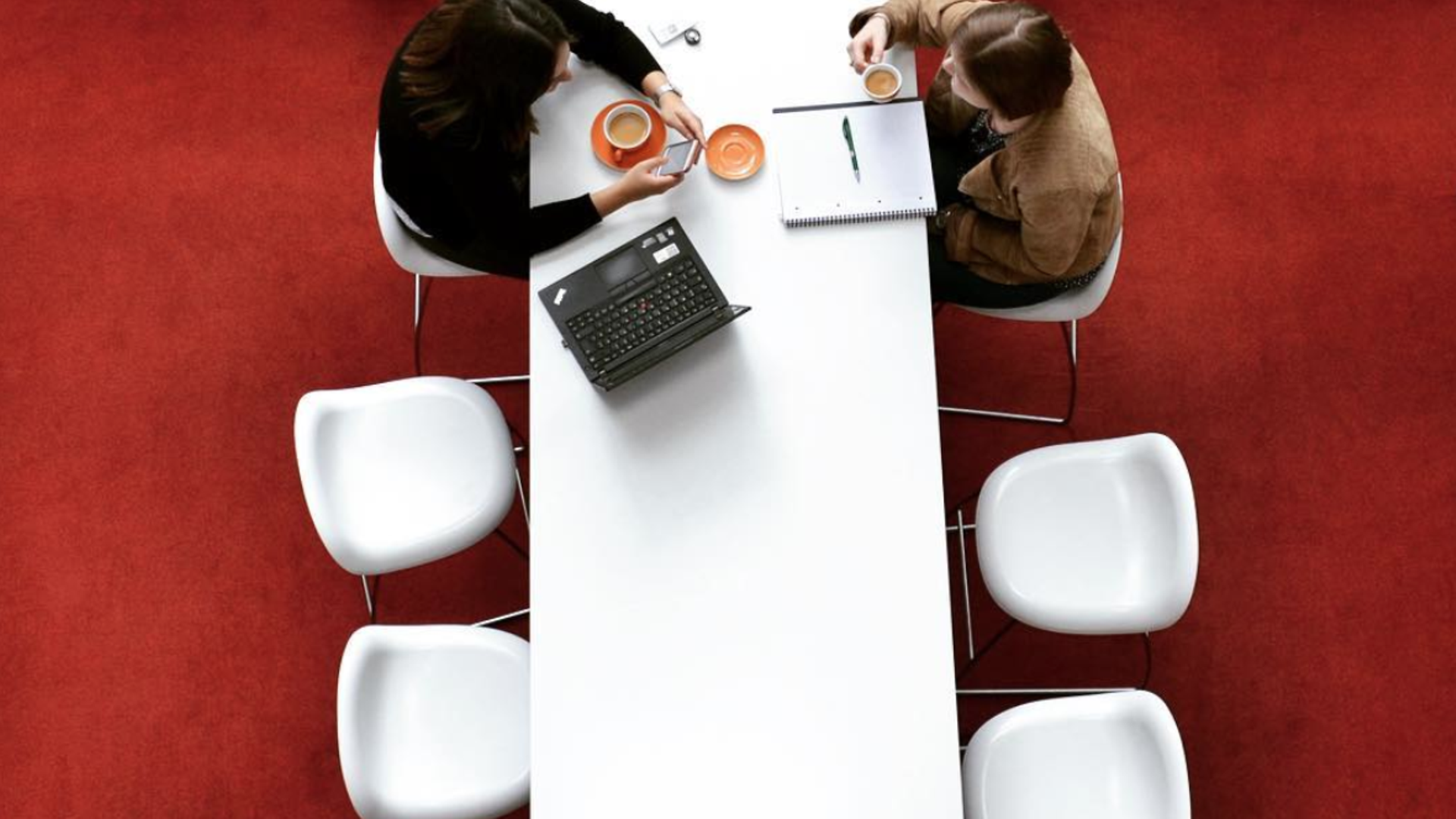 Foto desde arriba mostrando 2 empleados de Henkel sentados en una mesa blanca. 