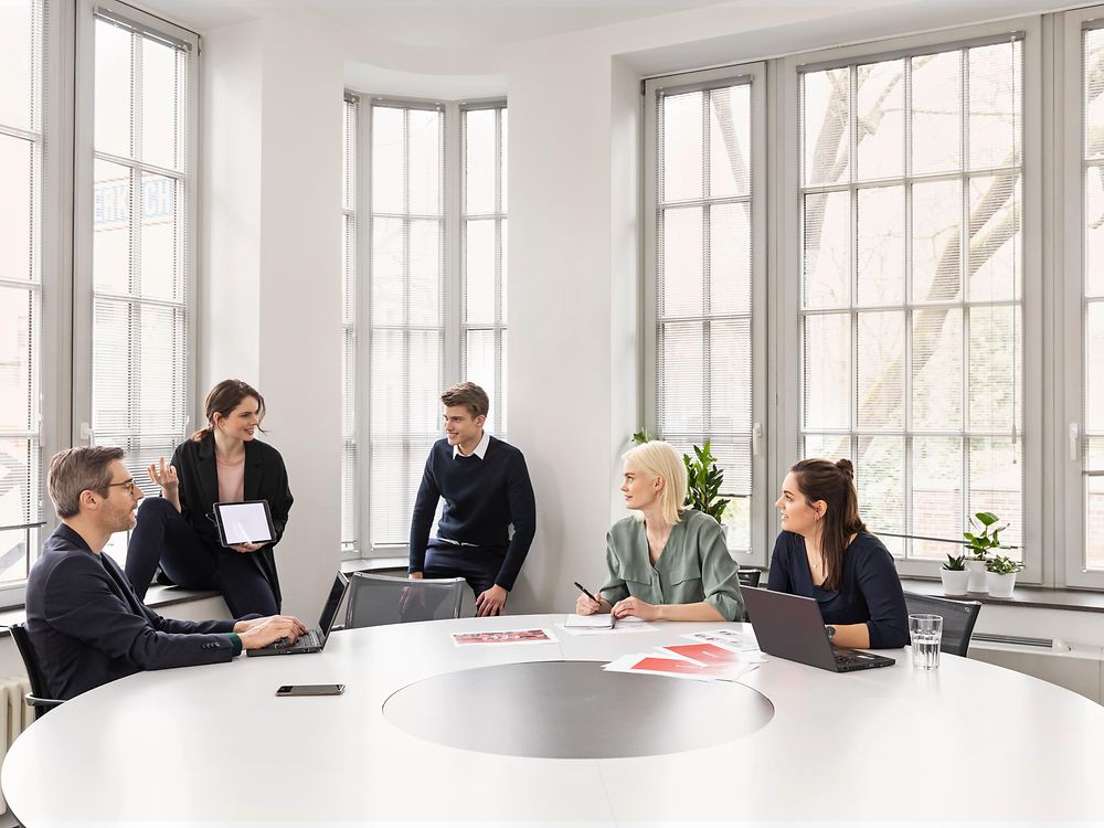 5 personas hablando entre ellos sentados alrededor de una mesa blanca en una sala de reuniones en Henkel con unas grandes ventanas 