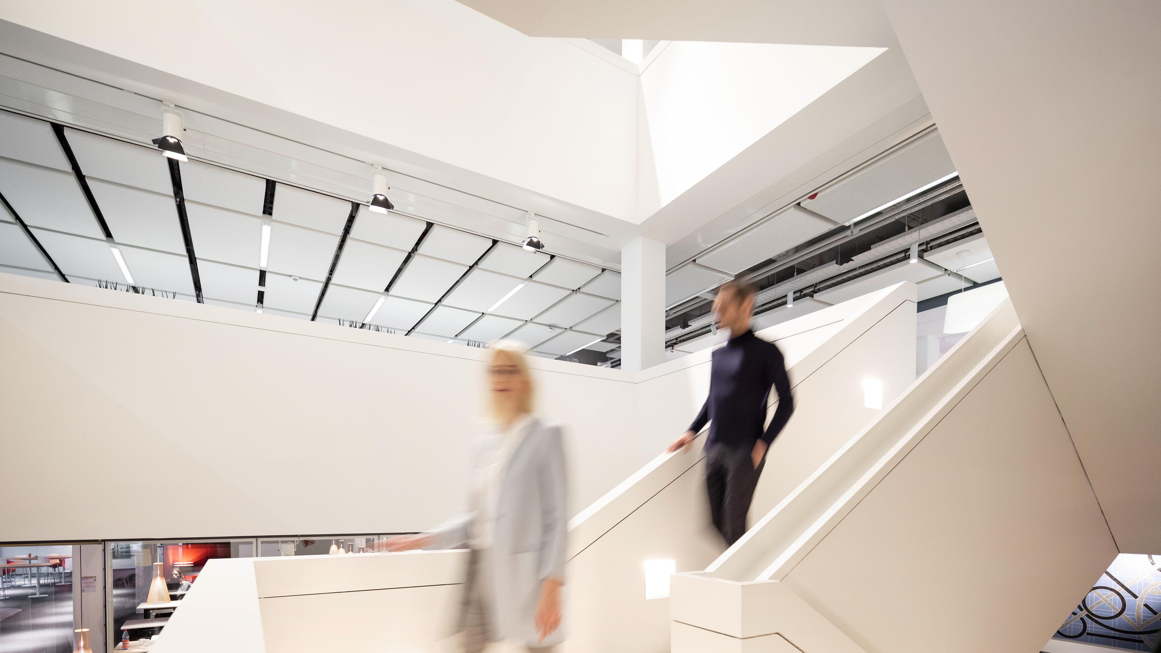 2 empleados de Henkel caminando hacia abajo de las escaleras blancas en las oficinas. 